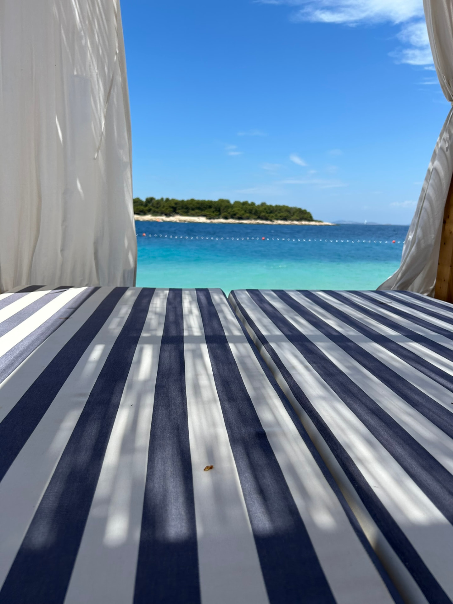 Blue and white striped cabana cushions with a view over the bay toward a pine-covered island in Primosten