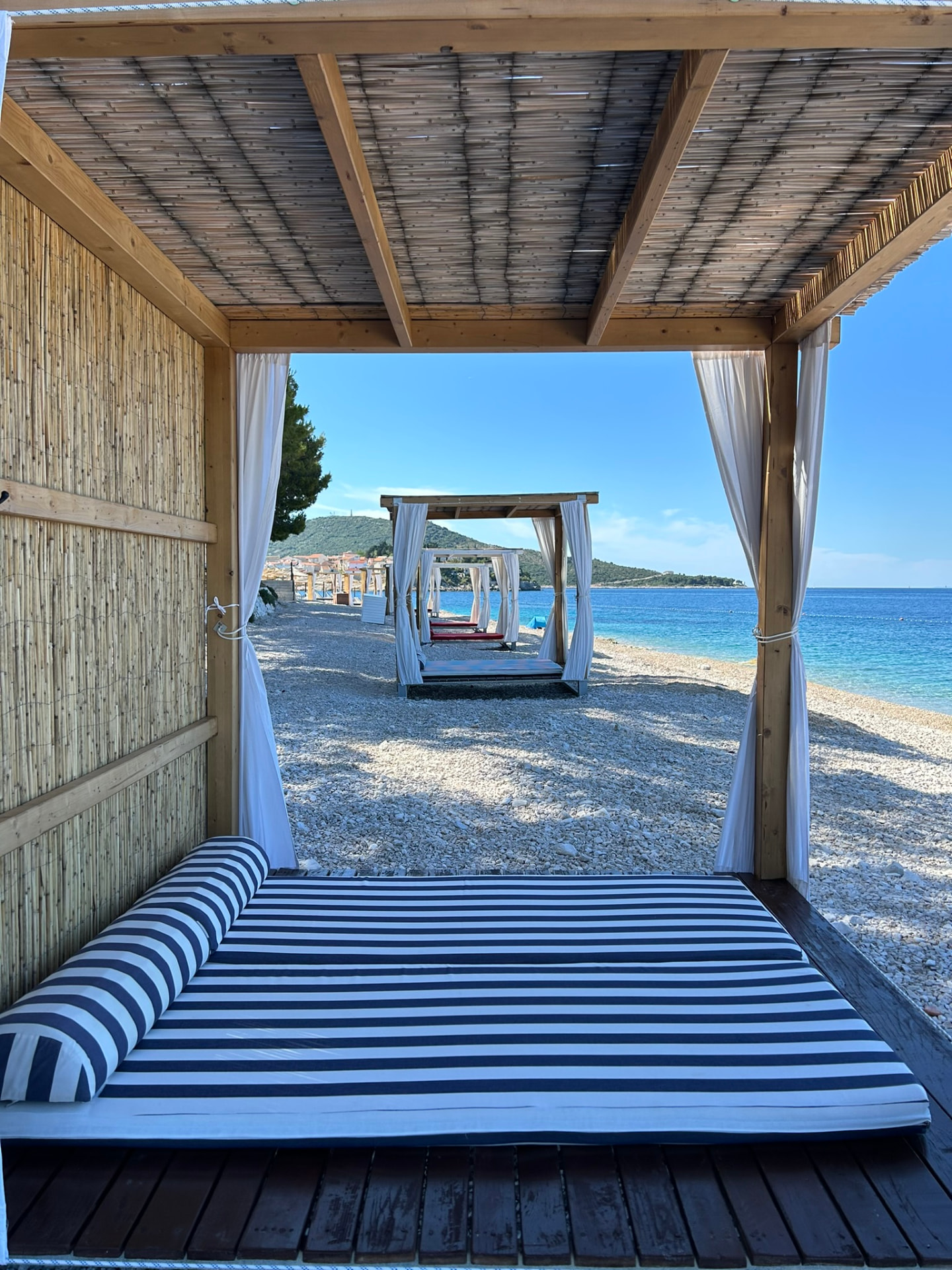 View of the sea from inside a Primosten Cabana beach cabana with striped cushions and light white curtains